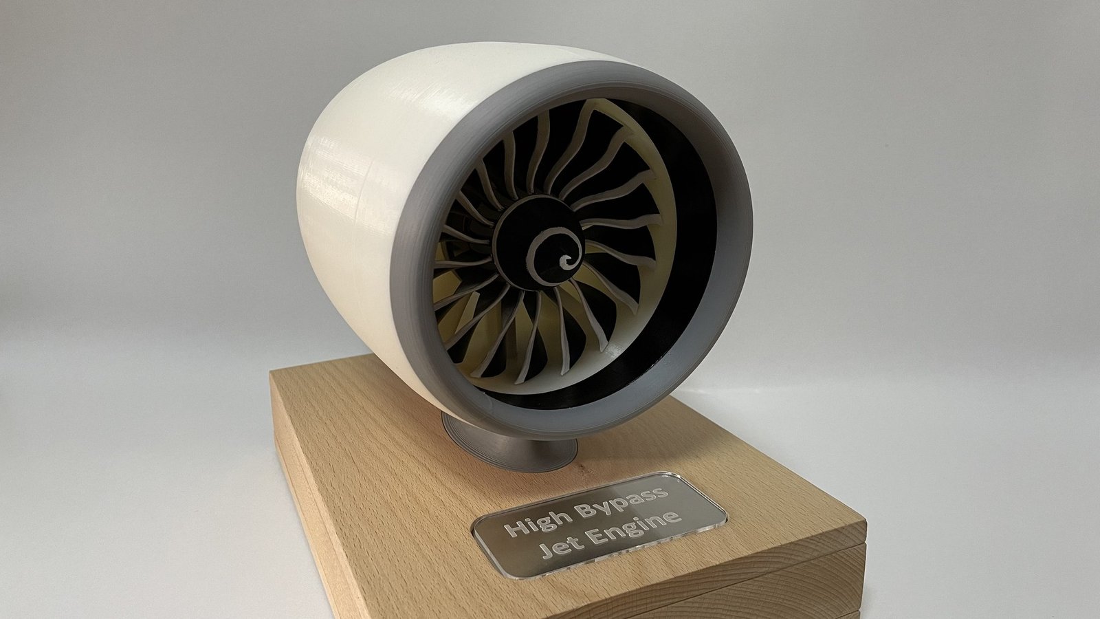 The finished engine on its wooden base, plaque in front, against a plain grey backdrop.