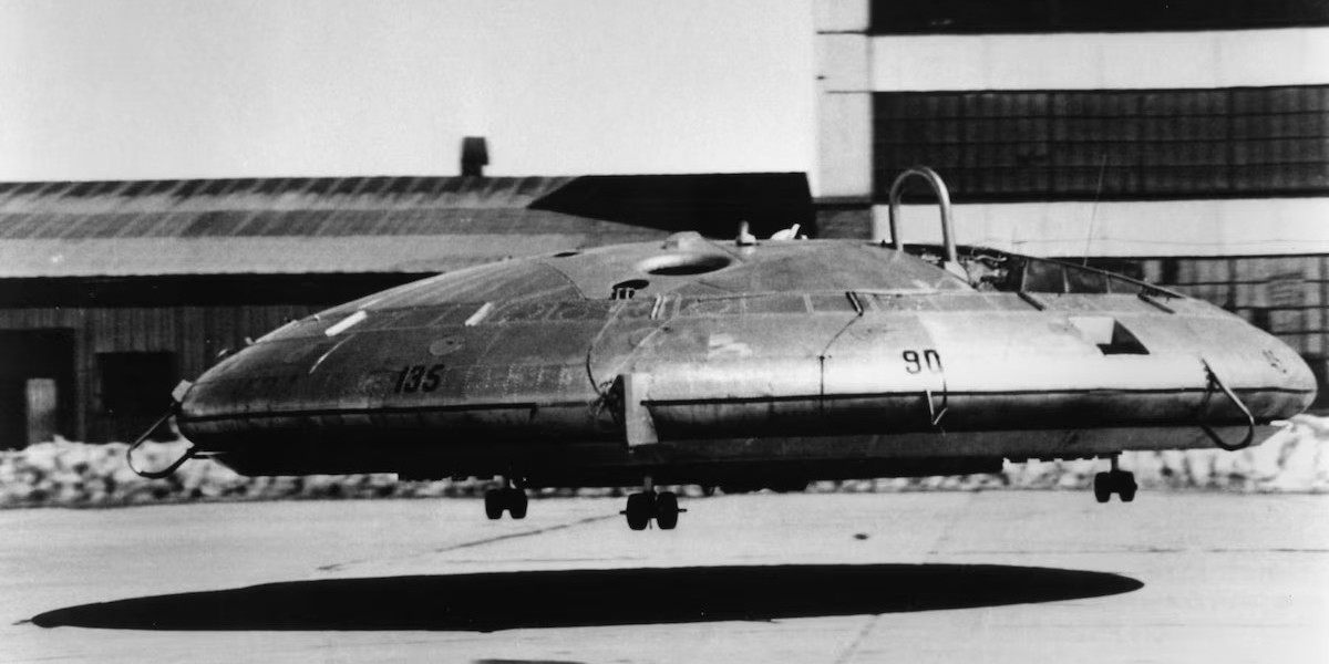 Black-and-white photograph of the Avro VZ-9 Avrocar hovering just above a runway beside a hangar.